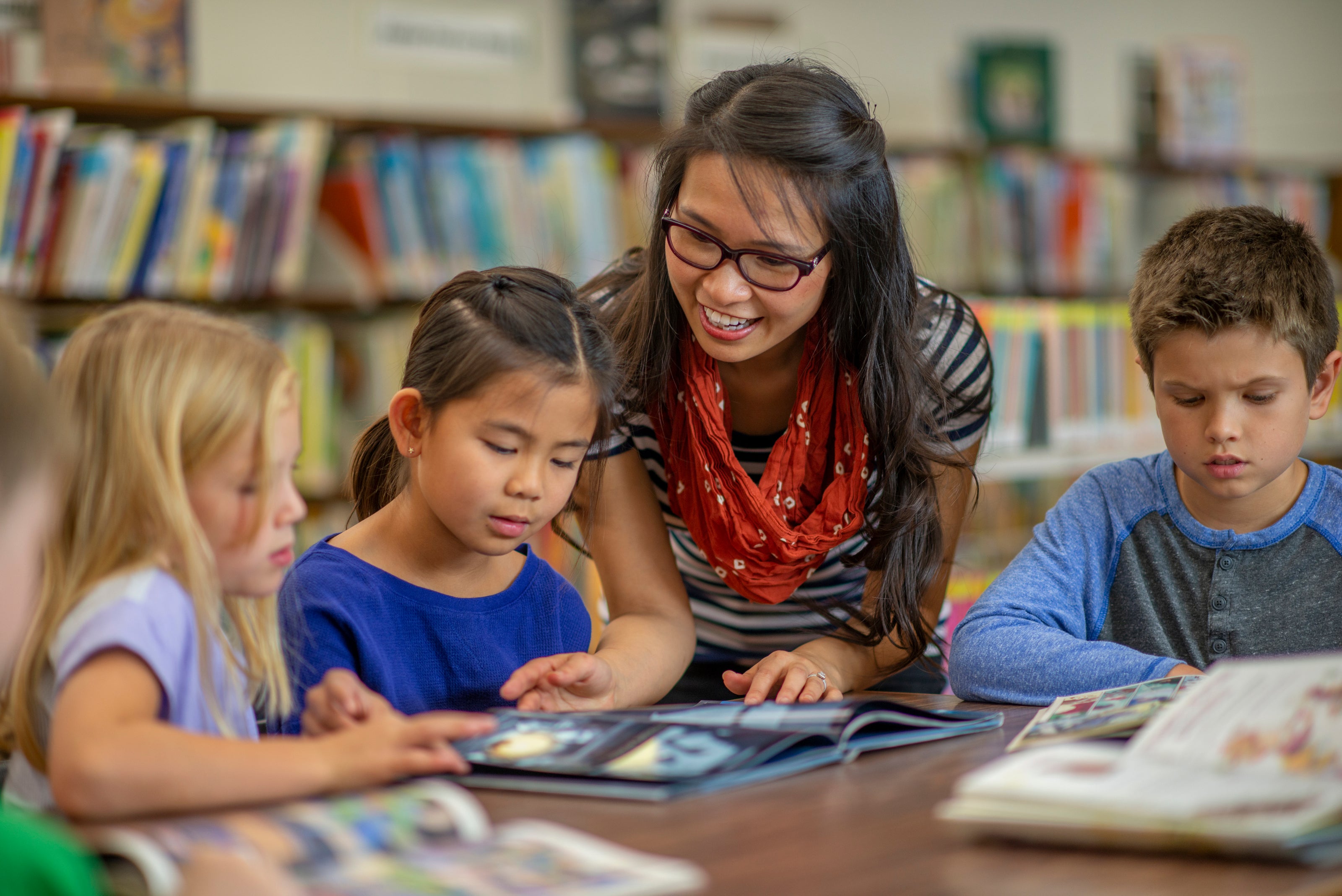 A teacher guides elementary students as they read picture books, fostering a love for reading. Explore our kids book club for engaging classroom reads!